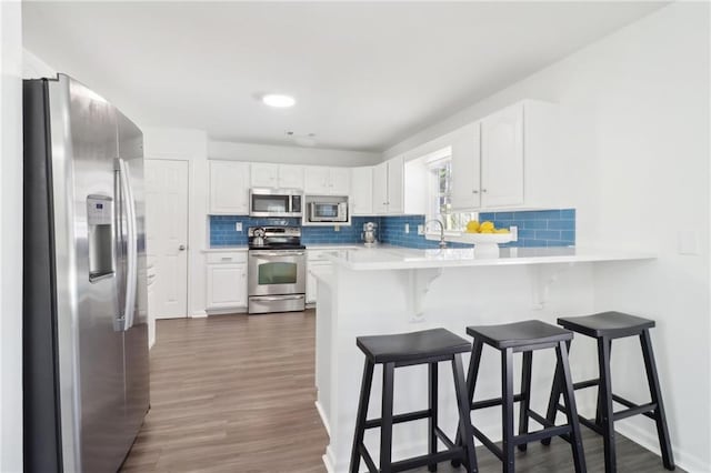 kitchen featuring stainless steel appliances, a peninsula, white cabinetry, light countertops, and a kitchen bar