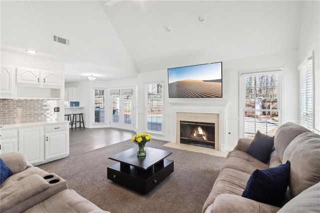 living area featuring a fireplace with flush hearth, visible vents, high vaulted ceiling, and wood finished floors