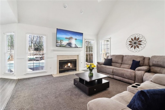 living room featuring high vaulted ceiling, a fireplace with flush hearth, and wood finished floors