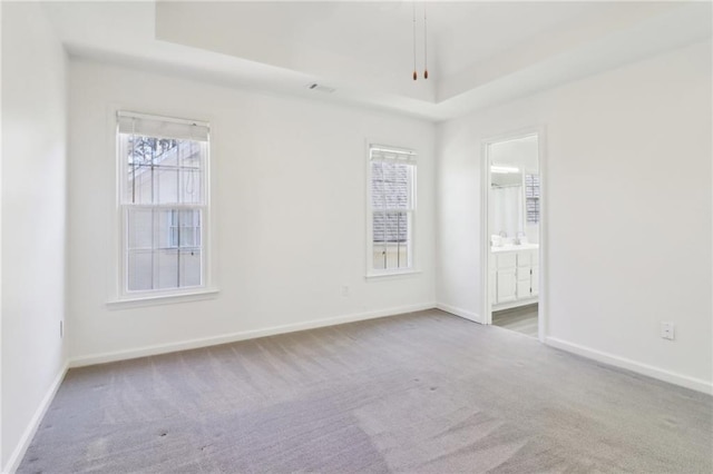 carpeted spare room with a tray ceiling and baseboards