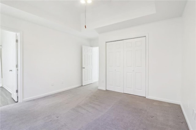 unfurnished bedroom with carpet floors, a closet, a raised ceiling, and baseboards