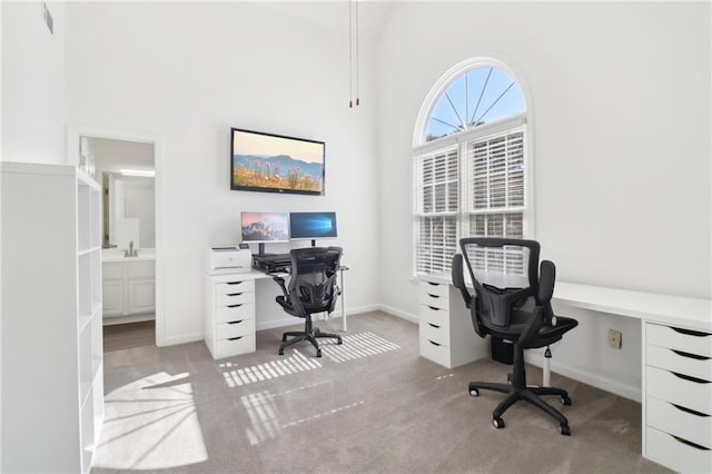 carpeted home office with visible vents, a towering ceiling, and baseboards