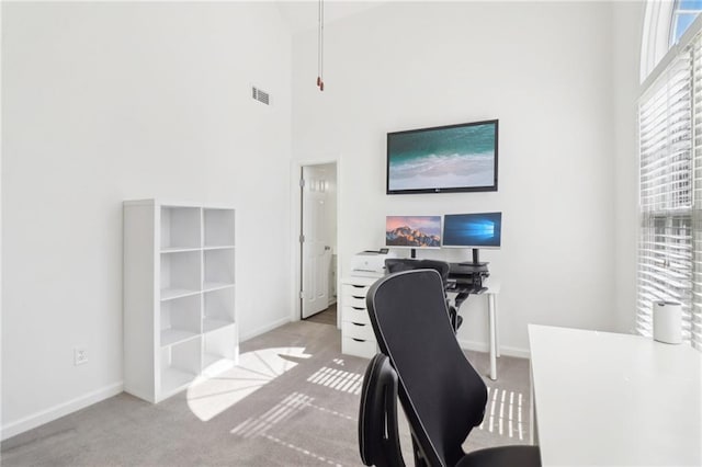 office featuring carpet, visible vents, a towering ceiling, and baseboards