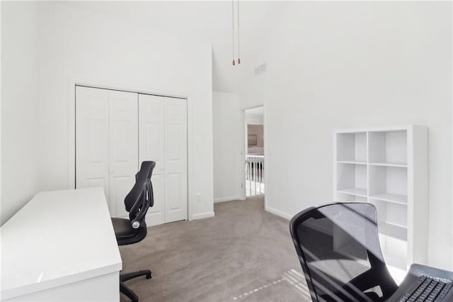 office space with carpet floors, visible vents, a towering ceiling, and baseboards