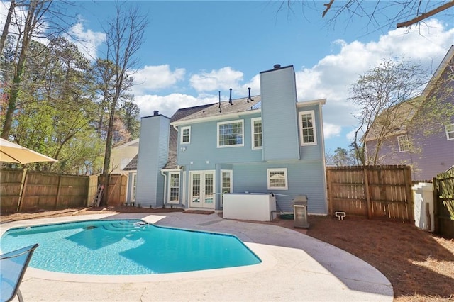 back of property featuring a fenced in pool, a fenced backyard, a chimney, french doors, and a patio area