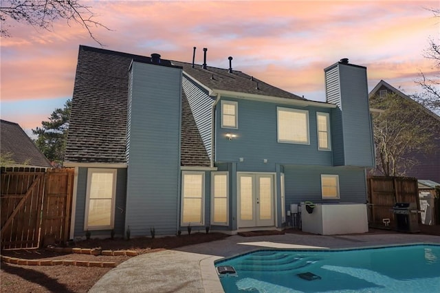 rear view of property with a chimney, fence, a fenced in pool, and french doors