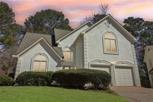 view of front of home with an attached garage, driveway, a yard, roof with shingles, and stucco siding