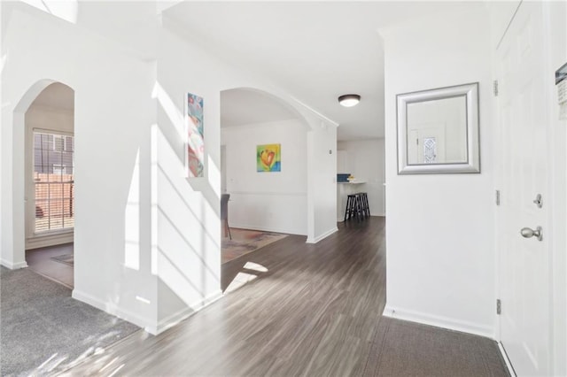 entrance foyer with arched walkways, baseboards, and wood finished floors