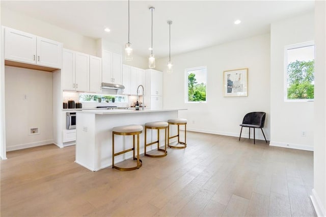 kitchen with a breakfast bar, white cabinets, light hardwood / wood-style flooring, an island with sink, and decorative light fixtures