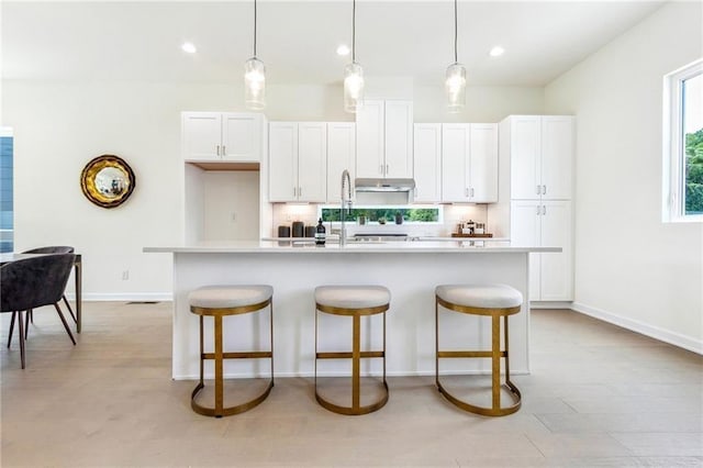 kitchen featuring backsplash, a center island with sink, white cabinets, and decorative light fixtures