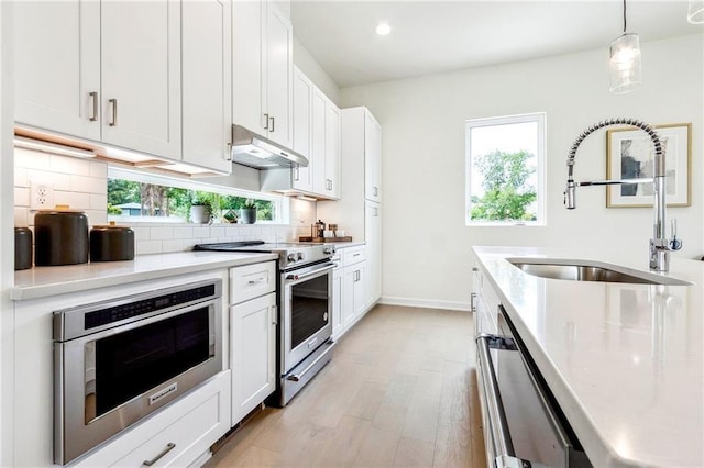 kitchen featuring appliances with stainless steel finishes, sink, decorative light fixtures, white cabinets, and light hardwood / wood-style floors