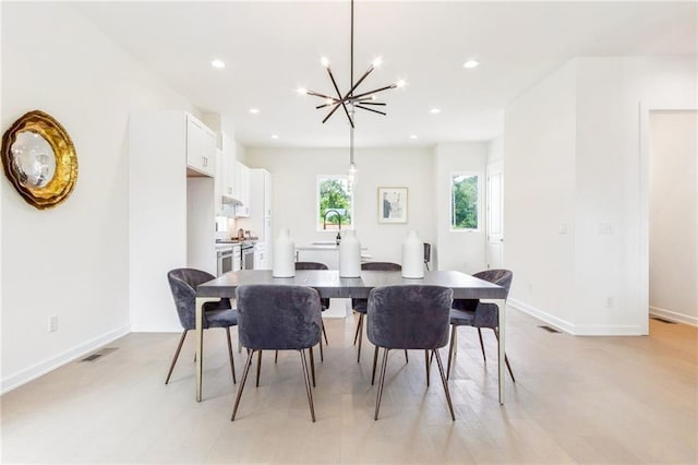 dining space featuring sink, light wood-type flooring, and an inviting chandelier