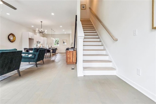 staircase featuring hardwood / wood-style floors and ceiling fan with notable chandelier