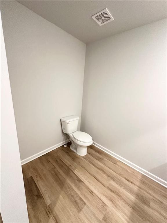 bathroom featuring toilet, wood finished floors, visible vents, and baseboards