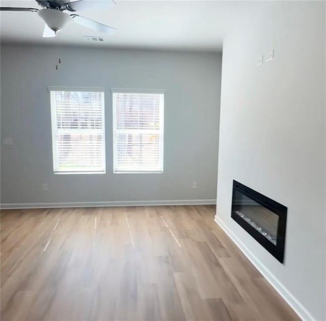 unfurnished living room with visible vents, baseboards, light wood finished floors, ceiling fan, and a glass covered fireplace