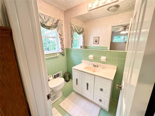 bathroom with toilet, tile patterned flooring, vanity, tile walls, and a textured ceiling