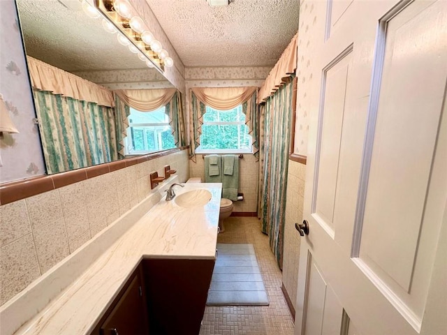 bathroom featuring a textured ceiling, toilet, tile patterned floors, tile walls, and vanity