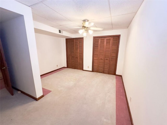 unfurnished bedroom featuring a paneled ceiling, multiple closets, carpet floors, and ceiling fan