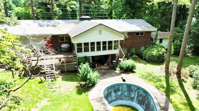 back of property with a deck, a lawn, and a sunroom