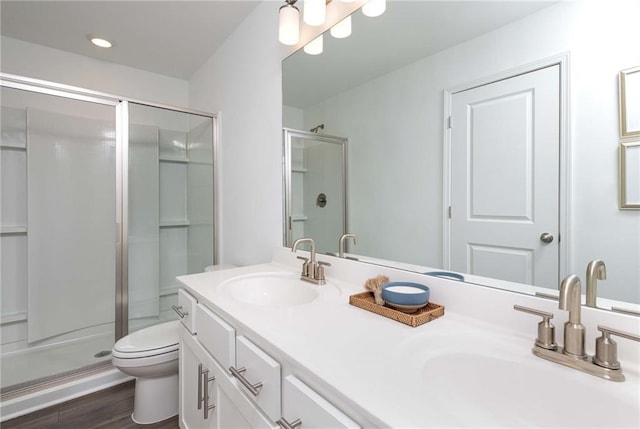bathroom with toilet, a stall shower, double vanity, and wood finished floors