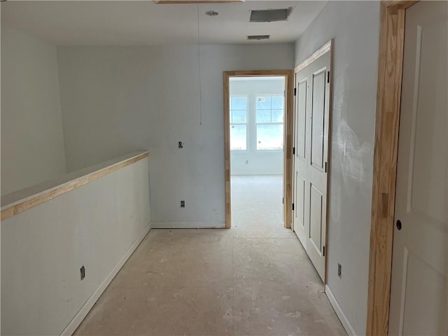corridor featuring concrete flooring and baseboards
