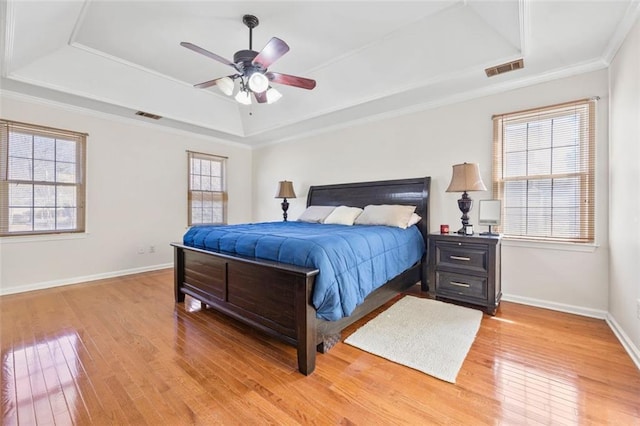 bedroom featuring visible vents, baseboards, a tray ceiling, light wood-style floors, and crown molding