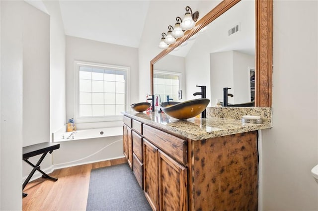 full bathroom with visible vents, a garden tub, a sink, wood finished floors, and lofted ceiling