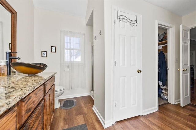 bathroom featuring vanity, wood finished floors, a stall shower, a spacious closet, and toilet