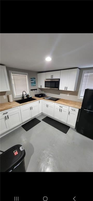 kitchen featuring concrete floors, black appliances, sink, and white cabinets