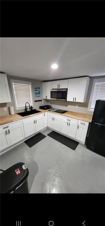 kitchen with concrete floors, sink, white cabinetry, and black appliances