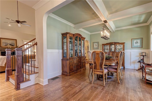 dining room featuring arched walkways, wood finished floors, stairs, and beam ceiling