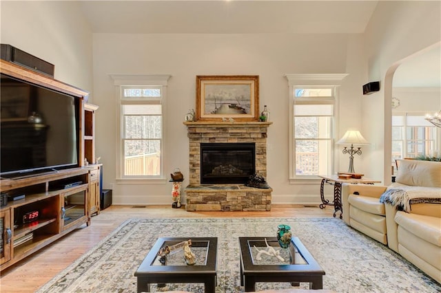 living room featuring light wood finished floors, a stone fireplace, arched walkways, and a healthy amount of sunlight