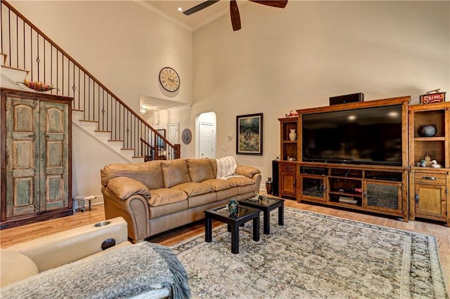 living room featuring arched walkways, stairway, crown molding, light wood-style floors, and high vaulted ceiling