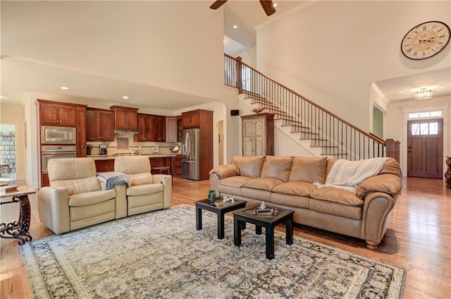 living room with arched walkways, crown molding, stairway, a ceiling fan, and light wood-type flooring