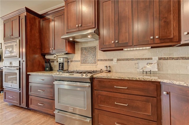 kitchen featuring stainless steel appliances, tasteful backsplash, light wood-style floors, light stone countertops, and under cabinet range hood