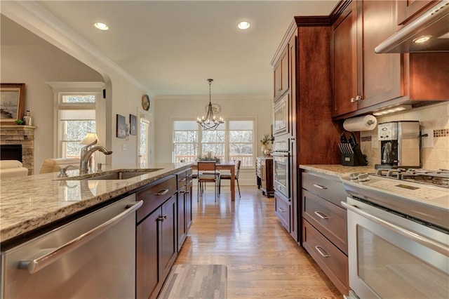 kitchen featuring stainless steel appliances, tasteful backsplash, a sink, light stone countertops, and exhaust hood