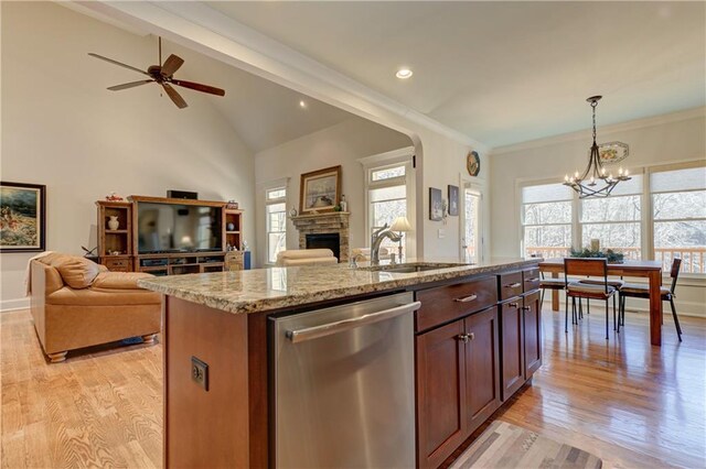 kitchen with an island with sink, open floor plan, a stone fireplace, pendant lighting, and stainless steel dishwasher