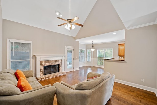 living room featuring high vaulted ceiling, crown molding, a brick fireplace, dark hardwood / wood-style floors, and ceiling fan