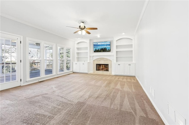 unfurnished living room featuring built in shelves, a fireplace, crown molding, light colored carpet, and baseboards