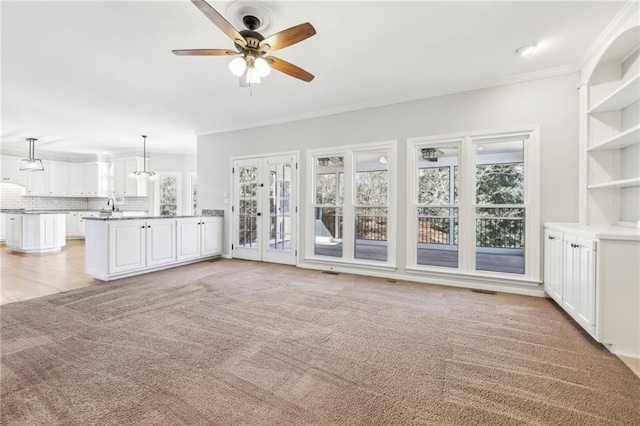 unfurnished living room featuring ornamental molding, light carpet, ceiling fan, and a sink