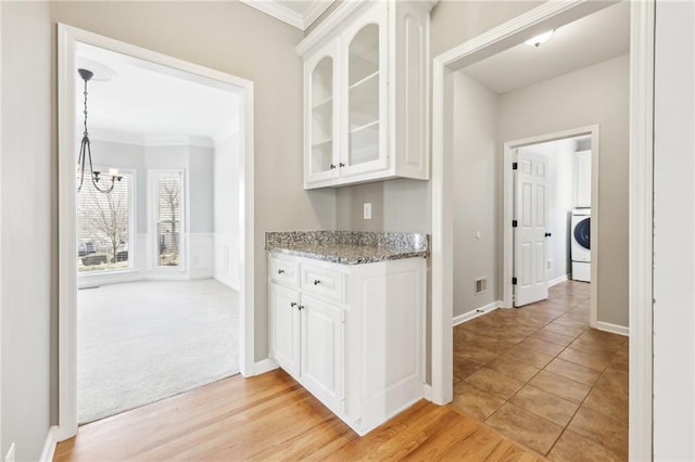 kitchen with washer / clothes dryer, glass insert cabinets, white cabinets, and ornamental molding