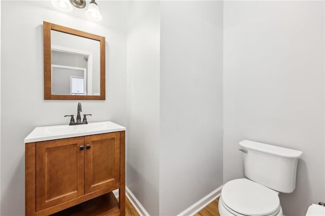 bathroom featuring toilet, baseboards, wood finished floors, and vanity