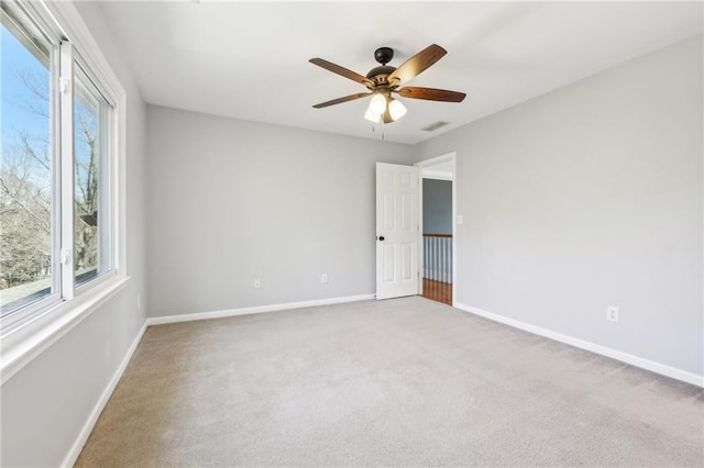 carpeted spare room with ceiling fan, visible vents, and baseboards