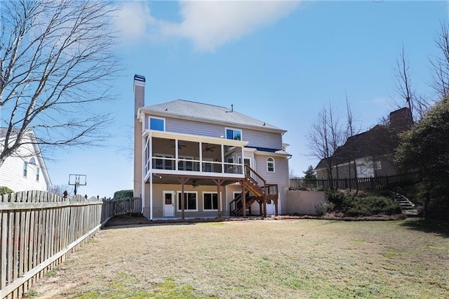 rear view of property featuring ceiling fan, a fenced backyard, a sunroom, a yard, and stairway