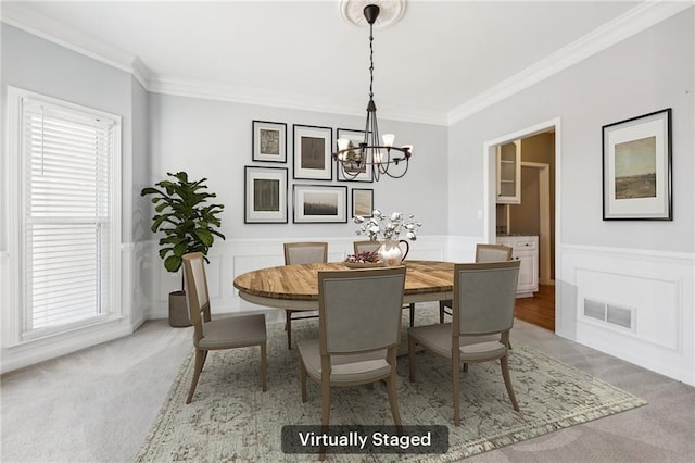 dining area with a chandelier, light colored carpet, a wainscoted wall, visible vents, and ornamental molding