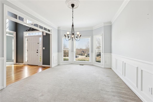 carpeted foyer with a wainscoted wall, a chandelier, a decorative wall, and ornamental molding