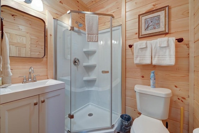 bathroom with vanity, wood walls, a stall shower, and toilet