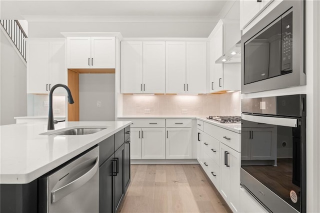 kitchen featuring appliances with stainless steel finishes, white cabinets, sink, light hardwood / wood-style floors, and decorative backsplash