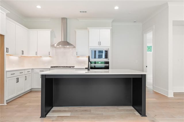 kitchen featuring wall chimney range hood, oven, black microwave, and white cabinets