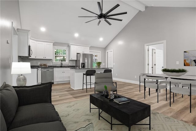 living room featuring ceiling fan, sink, beamed ceiling, high vaulted ceiling, and light hardwood / wood-style floors